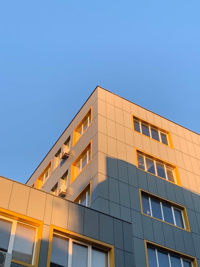 A modern office building with yellow accents under a clear blue sky, basking in sunlight.